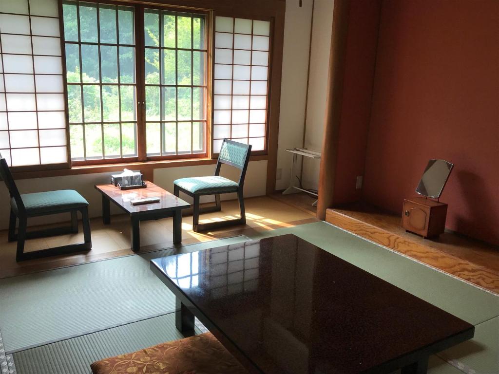A tatami guest room with two chairs by a shoji-screened window, a low table, and a raised alcove with a mirror stand