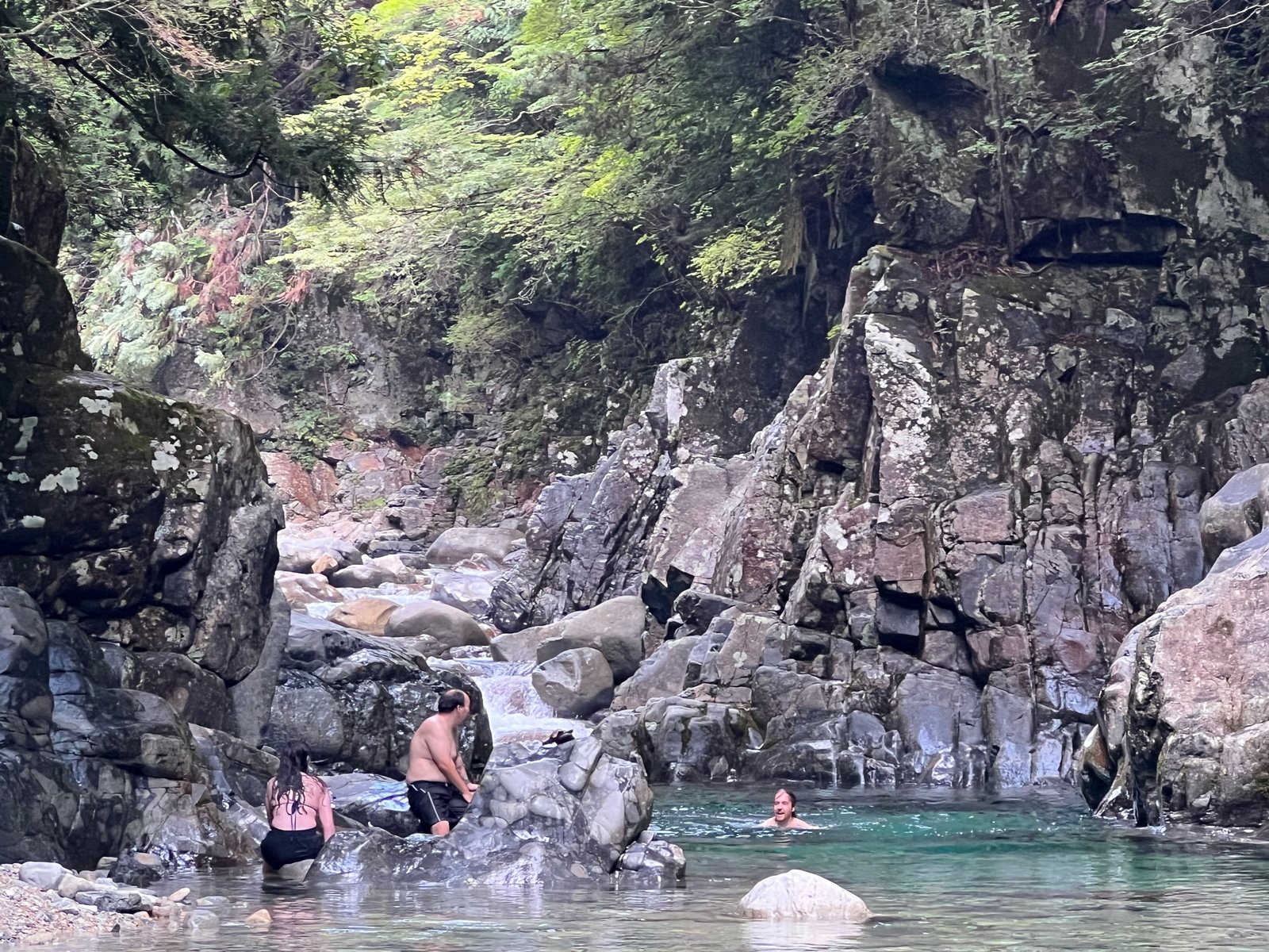 Guests wading and swimming into a clear turquoise pool between rocky canyon walls