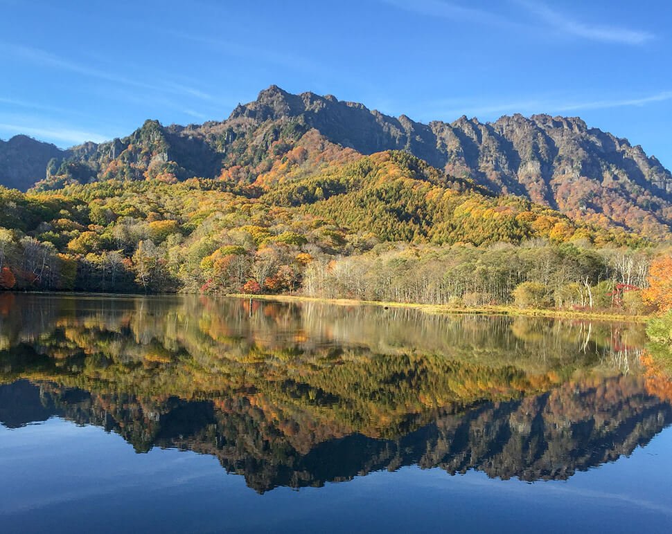 Mt. Togakushi's jagged rock face reflected in the still autumn waters of Kagami-ike (Mirror Pond)