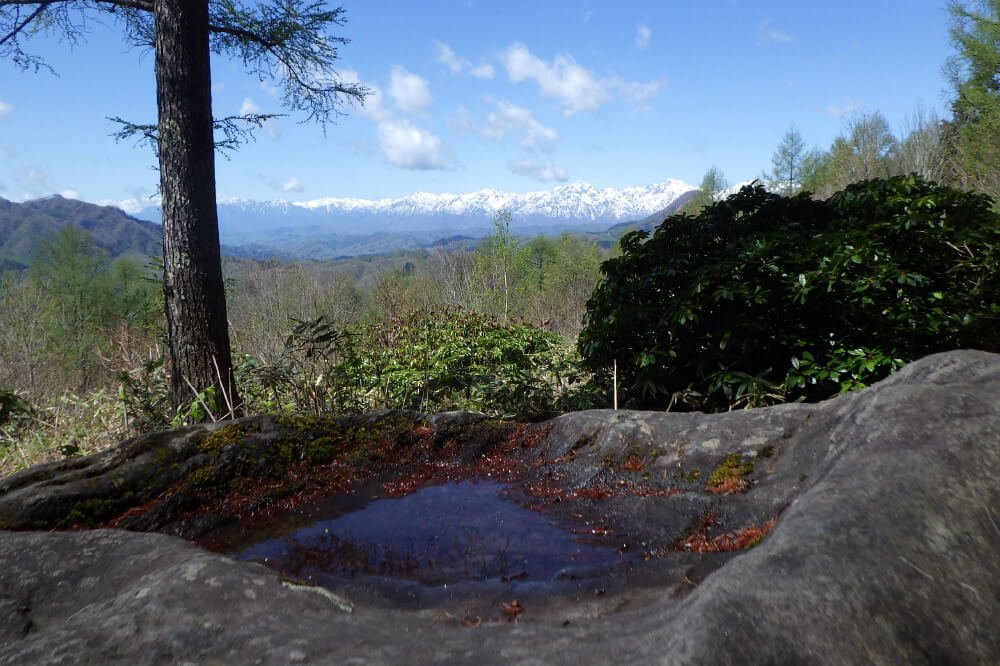 A rock outcrop along the Togakushi Kodo trail, with the snow-capped Northern Alps visible in the distance
