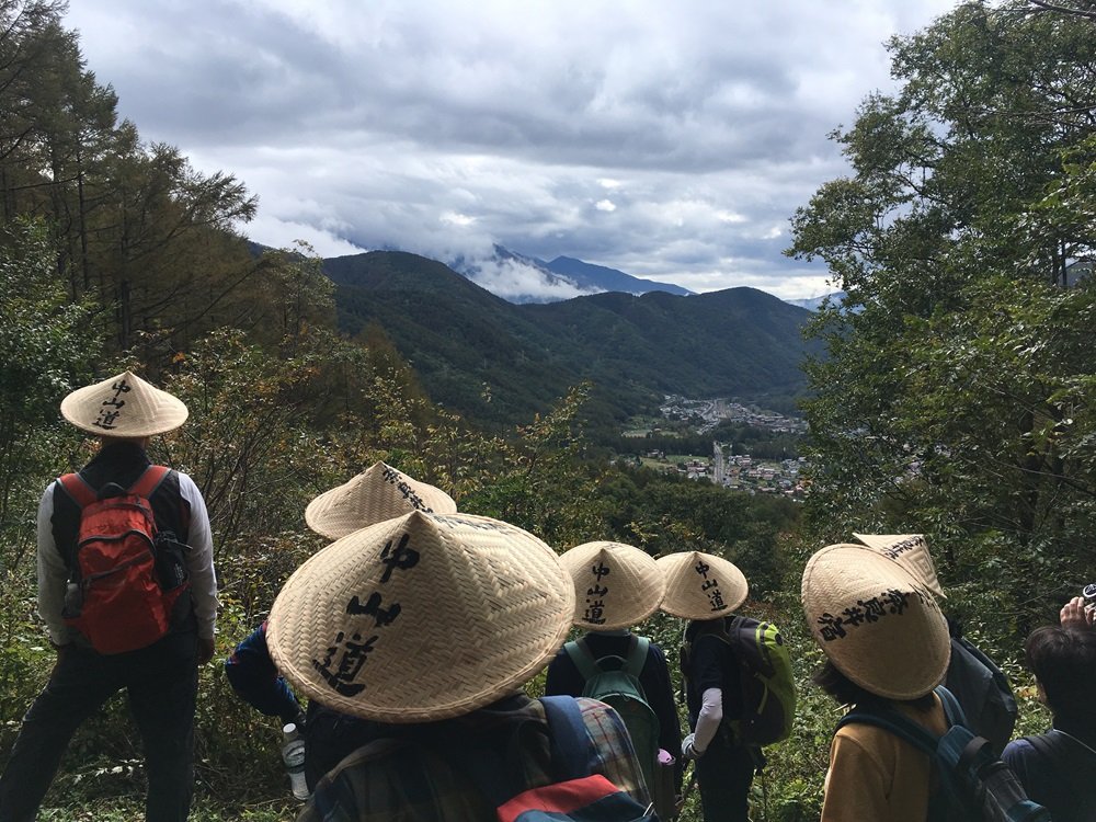 Hikers in traditional sedge hats pausing at an overlook on the Torii Pass trail