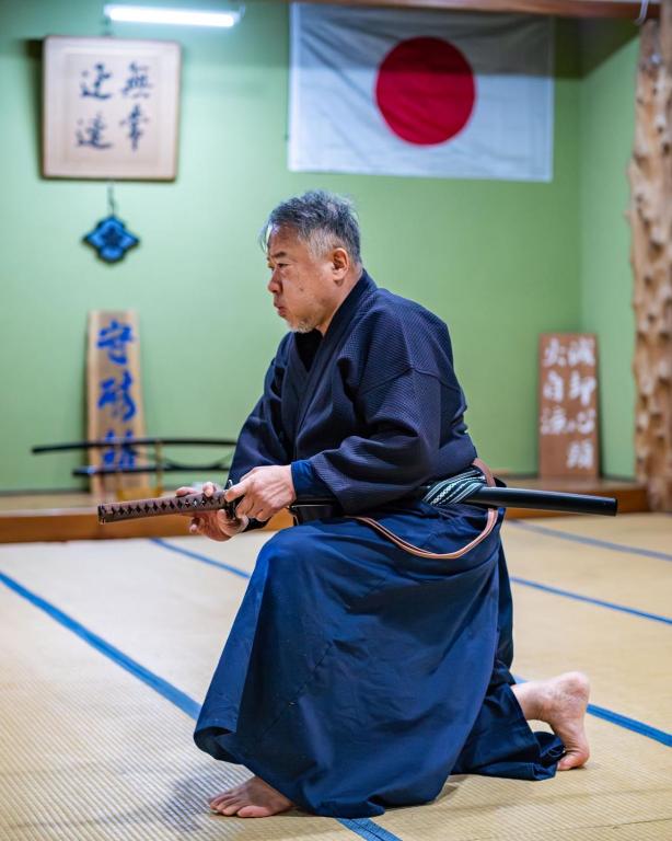 An instructor in hakama, kneeling with a katana in the dojo