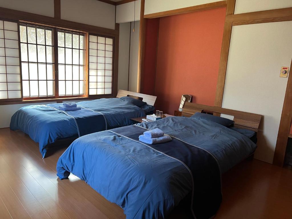 A renovated twin bed room with two beds made up with blue bedding and towels, beside a shoji-screened window